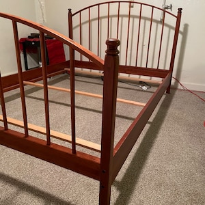 May include: A wooden bed frame with a curved headboard and slatted sides. The frame is made of dark wood and has a simple, classic design.