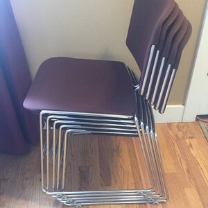 Puede incluir: Una pila de seis sillas burdeos con marcos cromados. Las sillas est&aacute;n apiladas en un patr&oacute;n escalonado, con los respaldos de las sillas mirando hacia la c&aacute;mara.