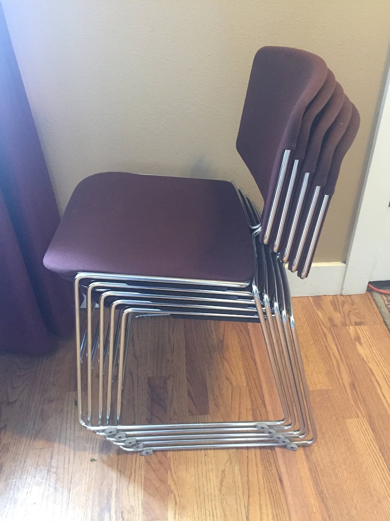 Puede incluir: Una pila de seis sillas burdeos con marcos cromados. Las sillas est&aacute;n apiladas en un patr&oacute;n escalonado, con los respaldos de las sillas mirando hacia la c&aacute;mara.