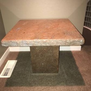 May include: A square, light brown, stone end table with a rough, textured surface. The table has a thick, solid base.