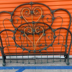 May include: Ornate, antique metal bed frame with a dark finish and gold accents. The headboard and footboard feature heart-shaped designs and decorative scrollwork, creating a vintage aesthetic.