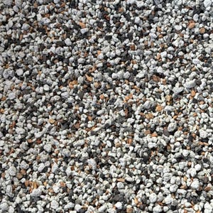 May include: A collection of small, irregular stones in a mix of white, light gray, dark charcoal, and earthy brown tones. The texture is rough and porous, with varying sizes of gravel creating a dense, multi-colored surface pattern throughout.