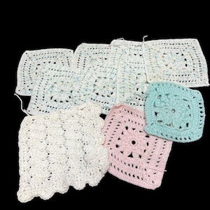 May include: A collection of handmade crochet squares in various colors, including white, light blue, and pink. The squares feature floral and geometric patterns, with a scalloped edge on one piece. The items are arranged on a black background.