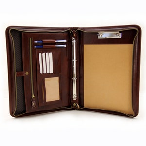 May include: Open brown leather zippered binder with a ring mechanism, a zippered pocket, a card slot, and a clipboard. The binder has a brown felt lining.