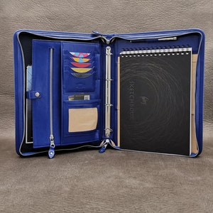May include: A blue leather zippered binder with a black sketchbook inside. The binder has multiple pockets and card slots. The sketchbook has the words "Sketchbook" printed on the cover.