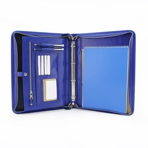 May include: A blue leather zippered binder with a notepad, pens, and card slots. The binder has a metal ring mechanism.