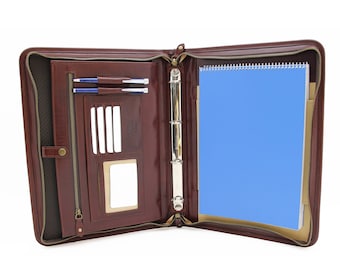 May include: Open brown leather business portfolio with a zipper closure. The interior features a blue spiral notebook, pen holders, card slots, and a small pocket. The portfolio is designed for organizing documents and accessories.