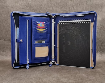 May include: A blue leather zippered binder with a black sketchbook inside. The binder has multiple pockets and card slots. The sketchbook has the words "Sketchbook" printed on the cover.