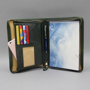 May include: A dark green leather zippered portfolio with a notepad, pen, and card slots. The notepad has a blue and white abstract design.
