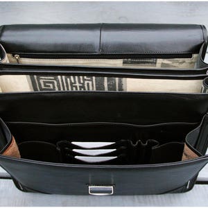 May include: A black leather briefcase with multiple compartments and a zippered closure. The briefcase has a strap and is open to reveal the interior.