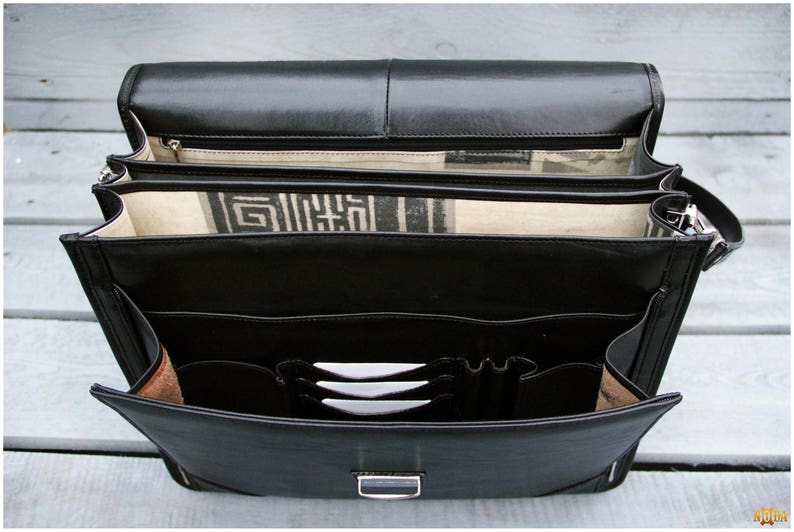 May include: A black leather briefcase with multiple compartments and a zippered closure. The briefcase has a strap and is open to reveal the interior.