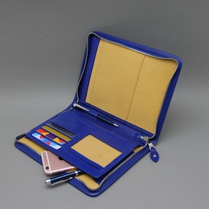 May include: A blue leather zippered wallet with a yellow interior. The wallet is open and has a phone, cards, and a pen inside.