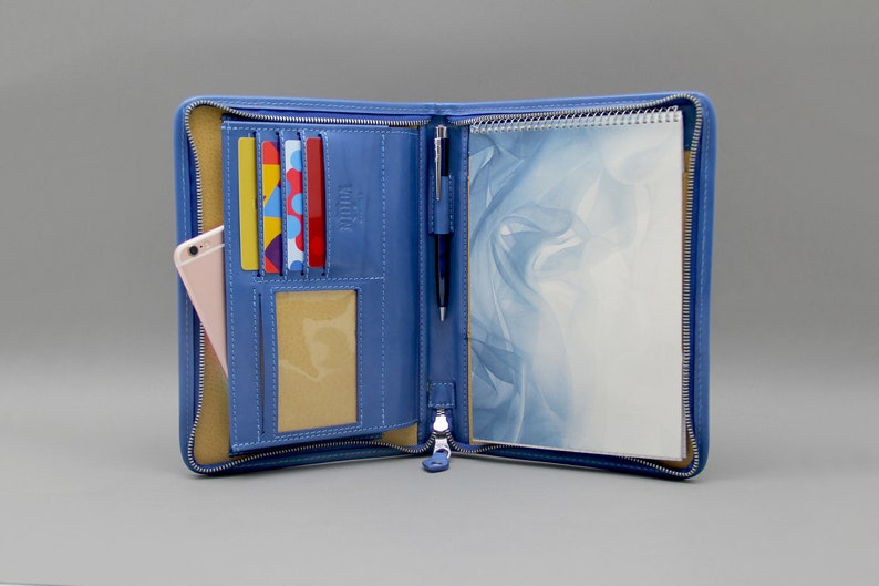 May include: A blue leather zippered portfolio with a notepad, pen holder, and card slots. The portfolio is open and the notepad is visible.