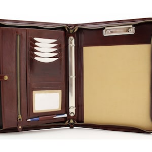 May include: A brown leather zippered binder with a ring mechanism, a pen holder, a card slot, and a clipboard. The binder is open and the interior is lined with a beige fabric.