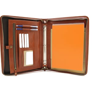 May include: A brown leather zippered portfolio with a built-in notepad and pen holders. The portfolio is open to reveal a notepad and pen slots.