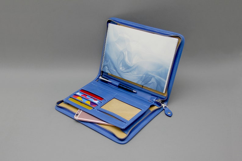 May include: A blue leather zippered travel wallet with multiple card slots, a pen holder, a phone pocket, and a clear ID window. The wallet is open and has a notebook inside.