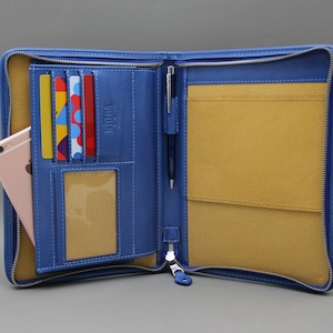 May include: A blue leather zippered portfolio with a pen holder, card slots, and a phone pocket. The interior is lined with a light brown fabric.