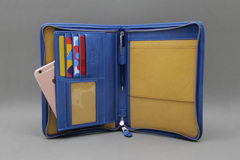 May include: A blue leather zippered portfolio with a pen holder, card slots, and a phone pocket. The interior is lined with a light brown fabric.