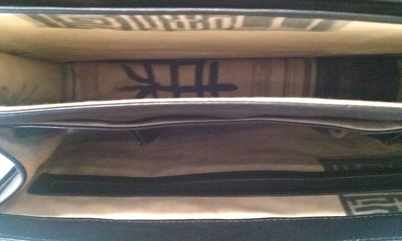 May include: Black leather bag with a zippered closure and a fabric lining. The bag is open and the lining is visible. The fabric lining has a pattern of black lines.