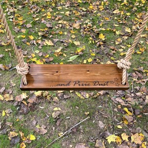 May include: A wooden swing set with rope hanging from the top. The swing seat is made of wood and has the words "...and Pixie Dust" engraved on it. There are three stars engraved on the right side of the seat.