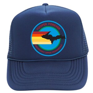 Puede incluir: Una gorra de camionero azul marino con un gráfico circular en la parte delantera. El diseño incluye una silueta negra de la península superior de Michigan sobre una franja horizontal con colores de atardecer, con el texto YOOPER FOREVER y MICHIGAN'S UPPER PENNINSULA.