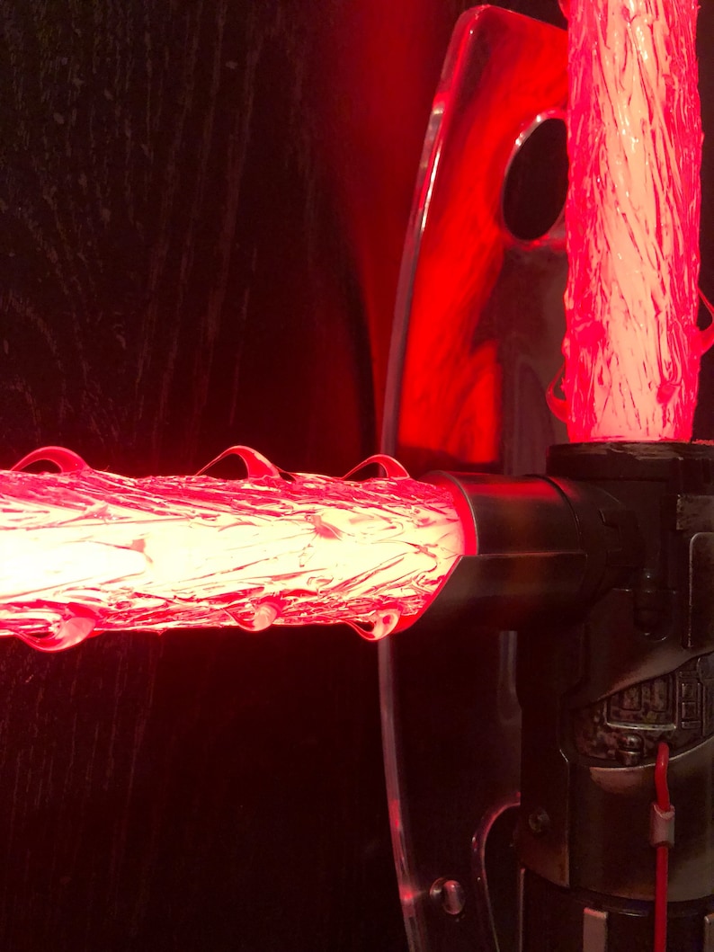 Op de afbeelding: Een rode lightsaber-prop met een transparante acrylstandaard. De lightsaber is aan en de blade is gemaakt van een doorschijnend materiaal.