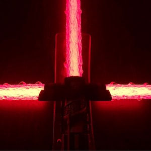 Op de afbeelding: Een rood lichtzwaard met een zwarte handgreep. Het lichtzwaard is aan en de kling gloeit.