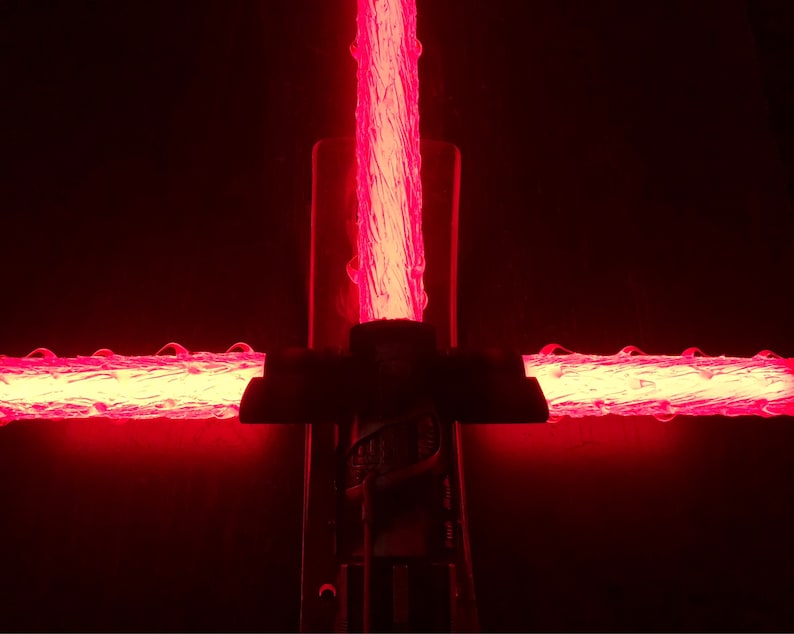 Op de afbeelding: Een rood lichtzwaard met een zwarte handgreep. Het lichtzwaard is aan en de kling gloeit.