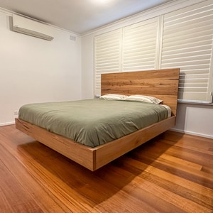 May include: A floating bed frame made of natural wood with a green duvet and two white pillows. The bed is in a bedroom with wood floors and white walls.
