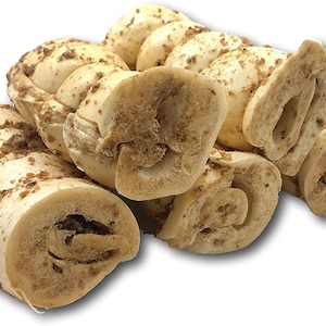 May include: A close-up of several beige dog chew treats. The treats are rolled into a spiral shape and have a brown, crunchy coating.