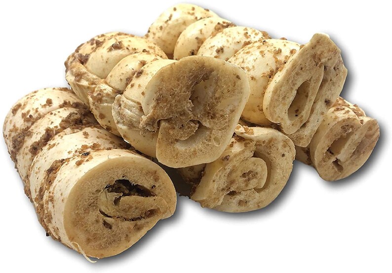 May include: A close-up of several beige dog chew treats. The treats are rolled into a spiral shape and have a brown, crunchy coating.