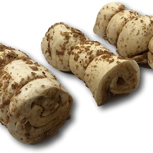 May include: Three dog chew toys made of rolled up, light brown, textured material. The chew toys are covered in brown crumbs.
