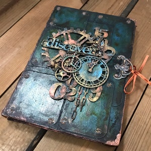 May include: A dark blue and green journal with a steampunk design. The cover features gears, clock faces, and the word "discover" with the numbers "02" and "15".