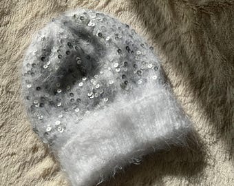 Śnieżnobiała, puszysta zimowa czapka z błyszczącymi srebrnymi cekinami – miękka, ciepła i stylowa