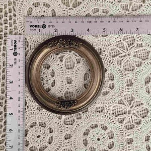 K&ouml;nnte beinhalten: Ein kleiner, runder Bilderrahmen im antiken Stil mit dunkelbraunem Finish und floralen Akzenten. Der Rahmen hat einen Durchmesser von etwa 7.6 cm und liegt auf einer geh&auml;kelten Tischdecke. Ein Lineal liegt neben dem Rahmen.