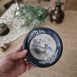 Peut inclure: Un petit cadre rond bleu avec une bordure argentée. Le cadre contient une impression florale vintage de roses blanches et de fleurs bleues.