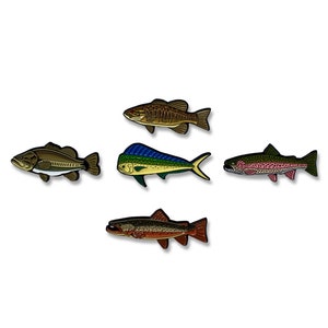 K&ouml;nnte beinhalten: F&uuml;nf Emaillestifte mit verschiedenen Fischarten. Die Stifte sind braun, blau, gr&uuml;n, rot und orange. Die Fische sind ein Barsch, ein Mahi-Mahi, eine Forelle und zwei andere Fischarten.