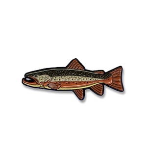 K&ouml;nnte beinhalten: Eine Emaille-Anstecknadel mit einem braunen und gr&uuml;nen Fisch, der eine Forelle darstellt, mit schwarzen Umrissen.