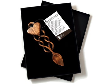 May include: A wooden lovespoon with a heart-shaped handle and a Celtic knot design. The spoon is in a black box with a tag that reads "The Welsh Lovespoon: Common Symbols & Meanings".
