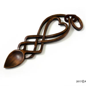May include: A wooden spoon carved in the shape of a Celtic knot with two hearts intertwined. The spoon is dark brown and has a smooth, polished finish.