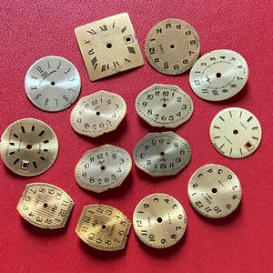 Puede incluir: Una colección de esferas de reloj antiguas de varias formas y tamaños, dispersas sobre una superficie roja. Las esferas presentan números romanos y arábigos, con algunas que muestran la marca "Luch" y "Zaria". Los colores son dorado, beige y plateado.