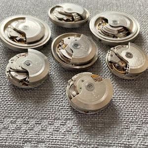 May include: A selection of dismantled watch movements, displaying intricate mechanical components. The silver parts reveal gears, springs, and other delicate elements, providing a view into the inner workings of timepieces.