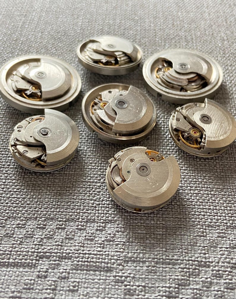 May include: A selection of dismantled watch movements, displaying intricate mechanical components. The silver parts reveal gears, springs, and other delicate elements, providing a view into the inner workings of timepieces.