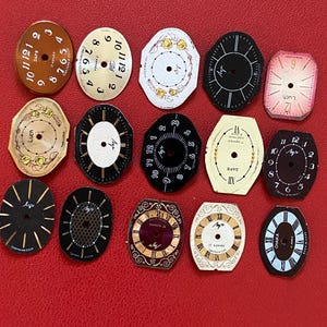 May include: A selection of antique watch dials in diverse shapes and hues, such as brown, black, white, and pink. The dials showcase Roman and Arabic numerals, with some incorporating floral patterns and text.