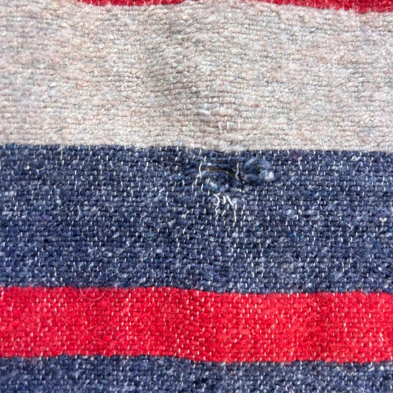Peut inclure: Gros plan sur un textile tiss&eacute; &agrave; rayures horizontales. Le motif pr&eacute;sente des bandes altern&eacute;es de rouge, bleu marine et blanc cass&eacute;. Le tissu a un aspect textur&eacute;, avec des fils visibles et une l&eacute;g&egrave;re imperfection dans la bande bleue.
