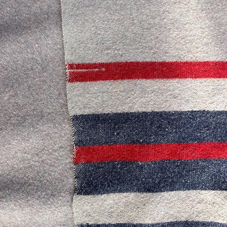 Peut inclure: Gros plan sur un textile tiss&eacute; avec un motif &agrave; rayures grises, rouges et bleu marine. Le tissu a un aspect textur&eacute;. Les rayures sont horizontales et espac&eacute;es uniform&eacute;ment, cr&eacute;ant un design classique.