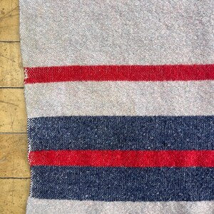 Peut inclure: Textile &agrave; rayures grises et rouges avec une texture tiss&eacute;e. Le motif pr&eacute;sente des bandes altern&eacute;es de gris, de rouge et de bleu marine. Le textile est probablement une couverture ou un plaid, avec une esth&eacute;tique rustique et vintage.