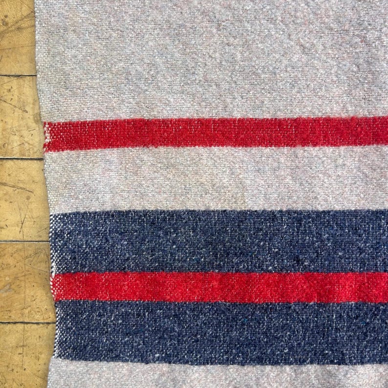Peut inclure: Textile &agrave; rayures grises et rouges avec une texture tiss&eacute;e. Le motif pr&eacute;sente des bandes altern&eacute;es de gris, de rouge et de bleu marine. Le textile est probablement une couverture ou un plaid, avec une esth&eacute;tique rustique et vintage.