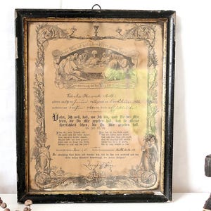 May include: A rectangular black wooden frame containing a vintage paper document with German text and a central illustration of the Last Supper. The document features ornate decorative borders, religious imagery, and handwritten details.