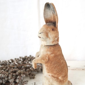 Può includere: Statuina di coniglio in piedi in stile vintage, nei toni del marrone e crema. Il coniglio ha lunghe orecchie e un piccolo collare. La statuina in materiale morbido è un oggetto decorativo, che ricorda i giocattoli antichi.